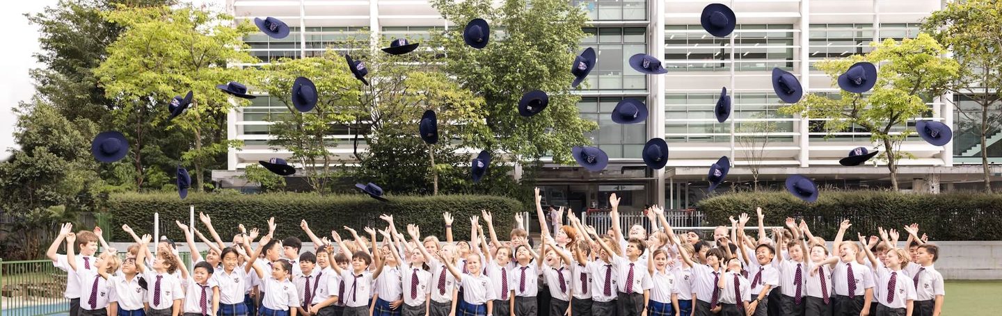 Prep pupils throwing their hats in the air in front of the Brighton College (Singapore) building