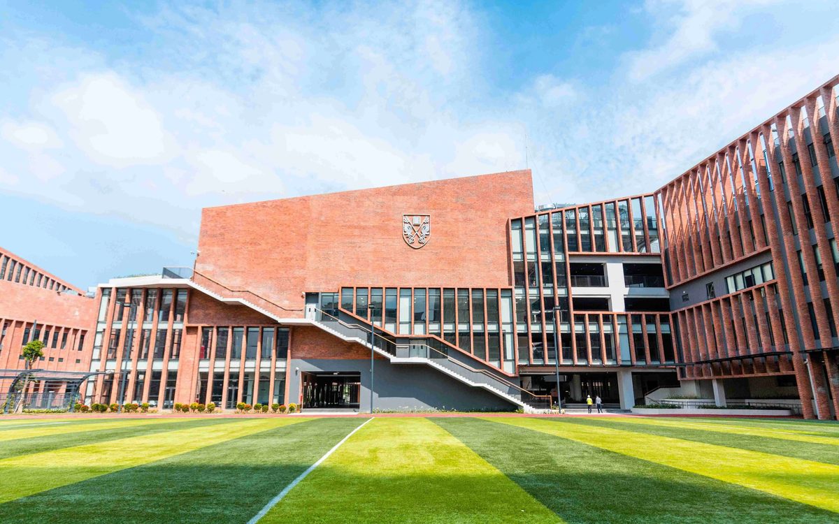 Red-brick main building of Brighton College Vietnam seen across the football pitch